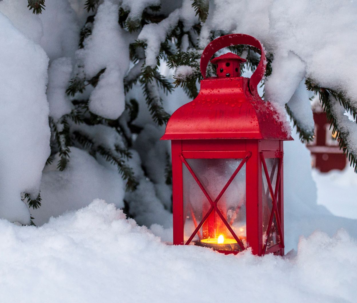 Punainen kynttilälyhty lumessa kuusen alla